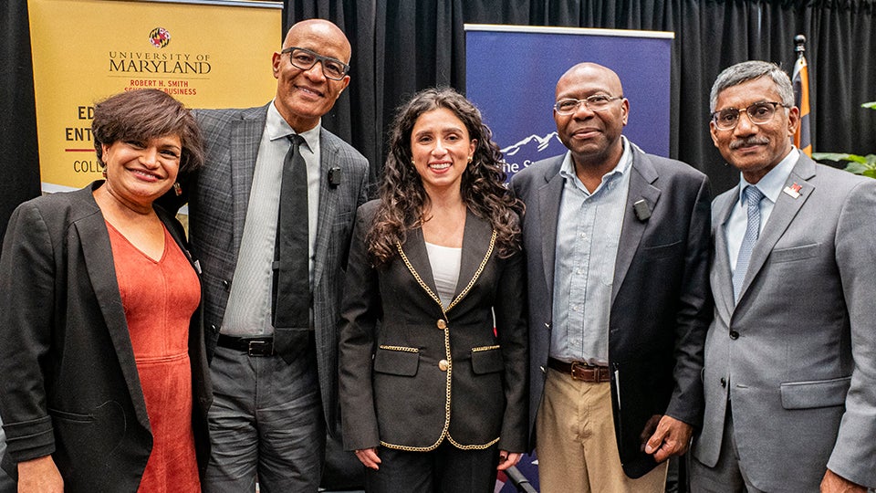 Five speakers and panelists pose smiling on-stage at the University of Maryland Smith School event on DEI policy debate.