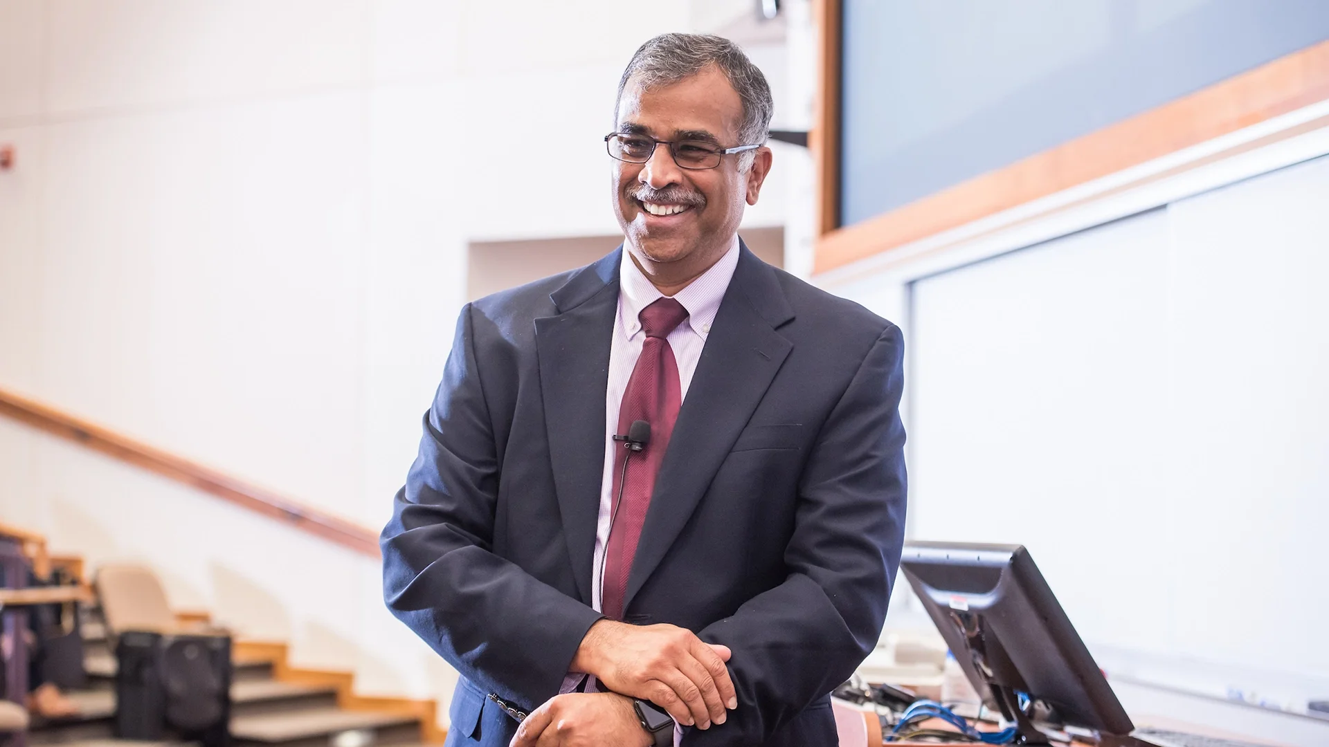 P.K. Kannan smiling while standing in a classroom, wearing a suit and tie.